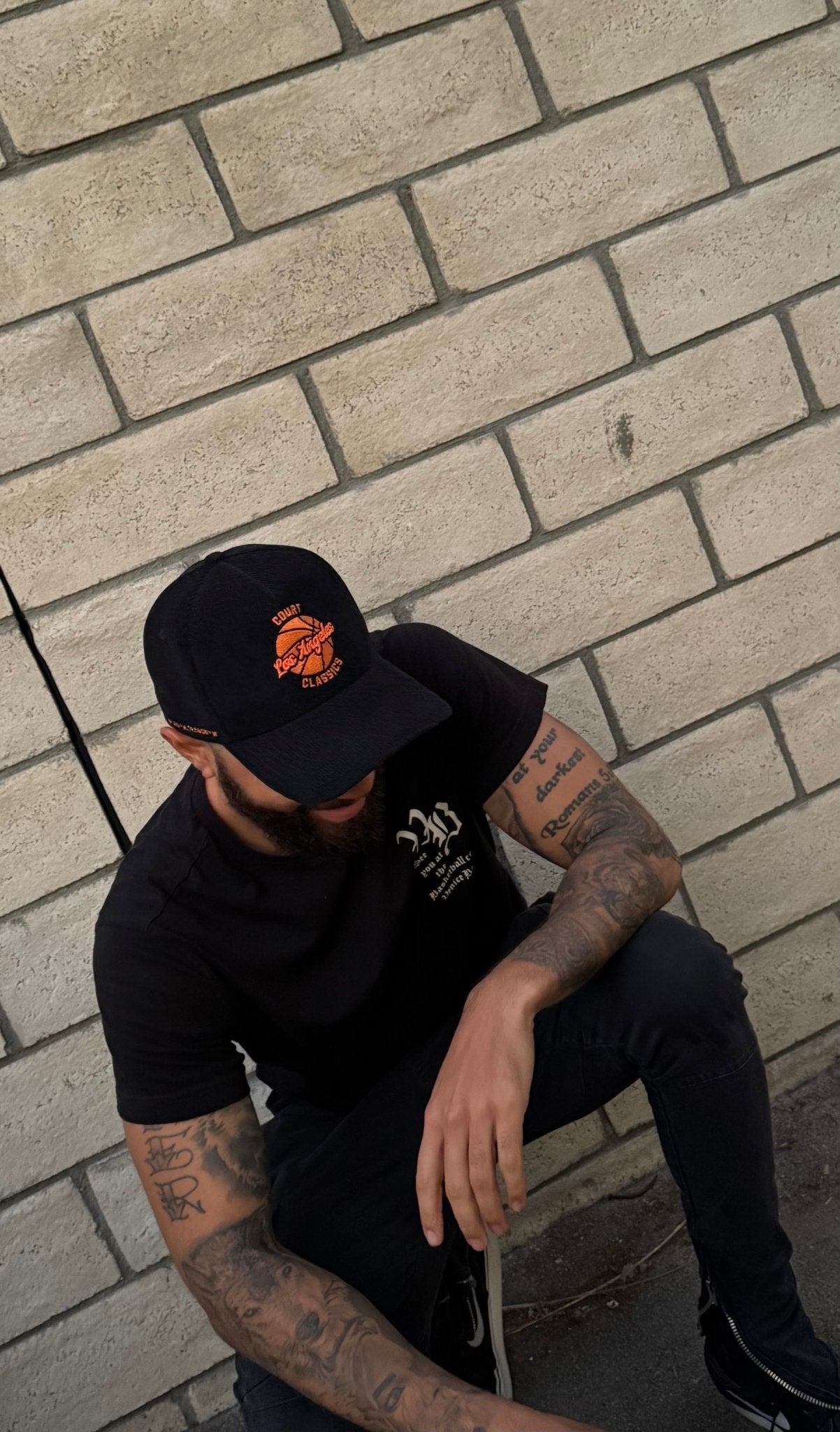 Streetwear style shot of black & orange corduroy snapback hat worn by man crouching near brick wall