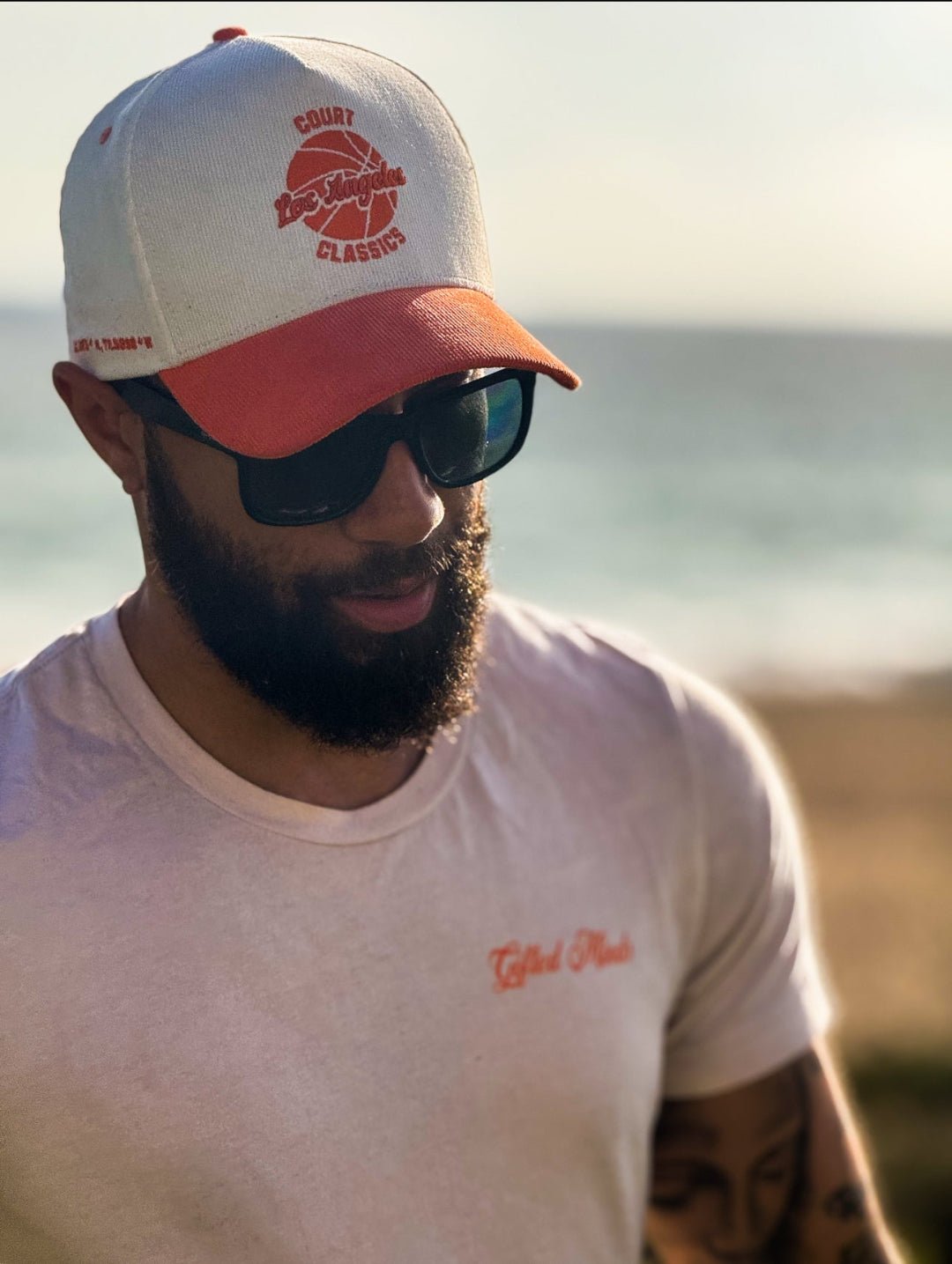 Model wearing white & orange corduroy snapback hat at sunset with palm trees – lifestyle shot